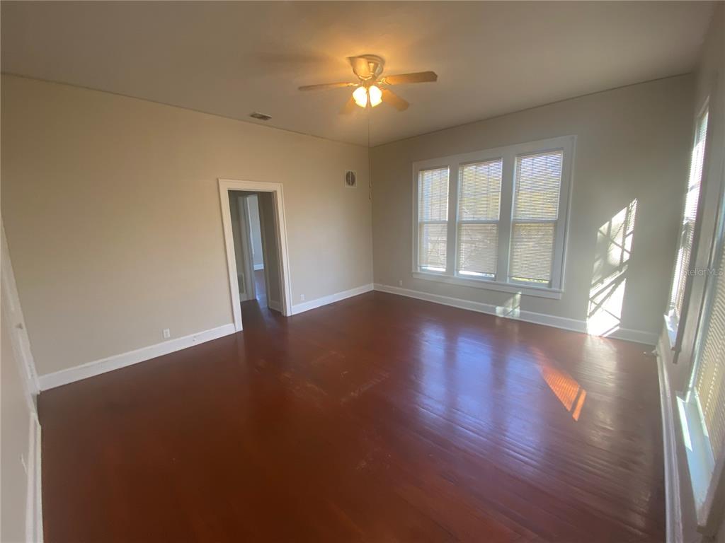 An empty room with hardwood floors, a ceiling fan, and large windows with blinds — 1120 WEBSTER STREET UNIT 4, LEESBURG, FL