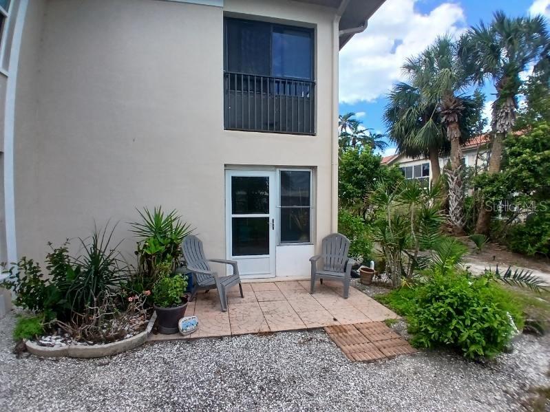 A ground-level patio with two chairs sits outside a building with a screened balcony above — 10350 IMPERIAL POINT DRIVE W UNIT 8, LARGO, FL