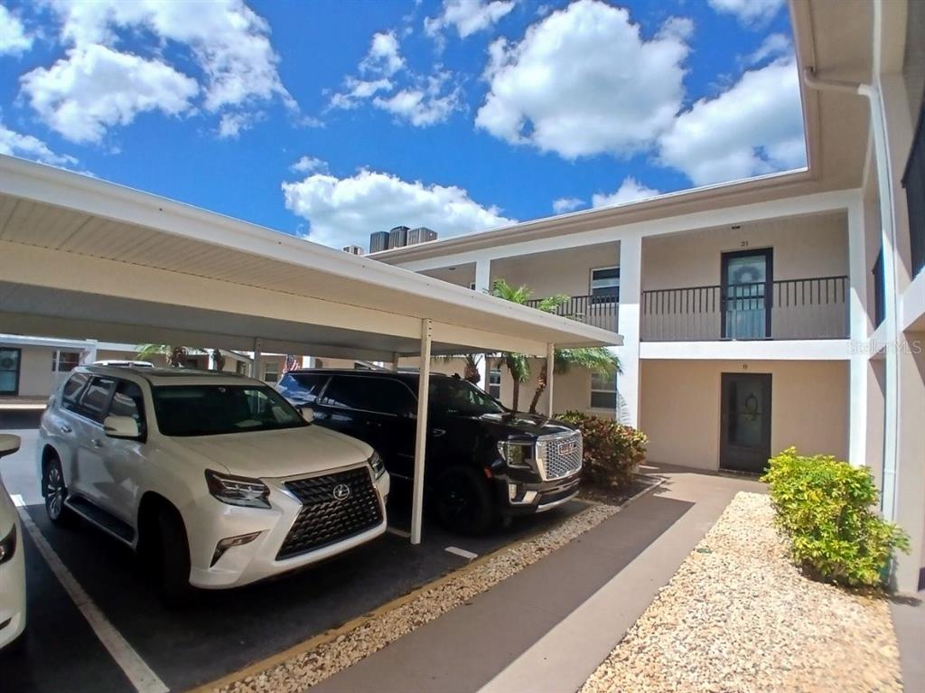 A white Lexus and a black SUV are parked under a carport beside an apartment building — 10350 IMPERIAL POINT DRIVE W UNIT 8, LARGO, FL