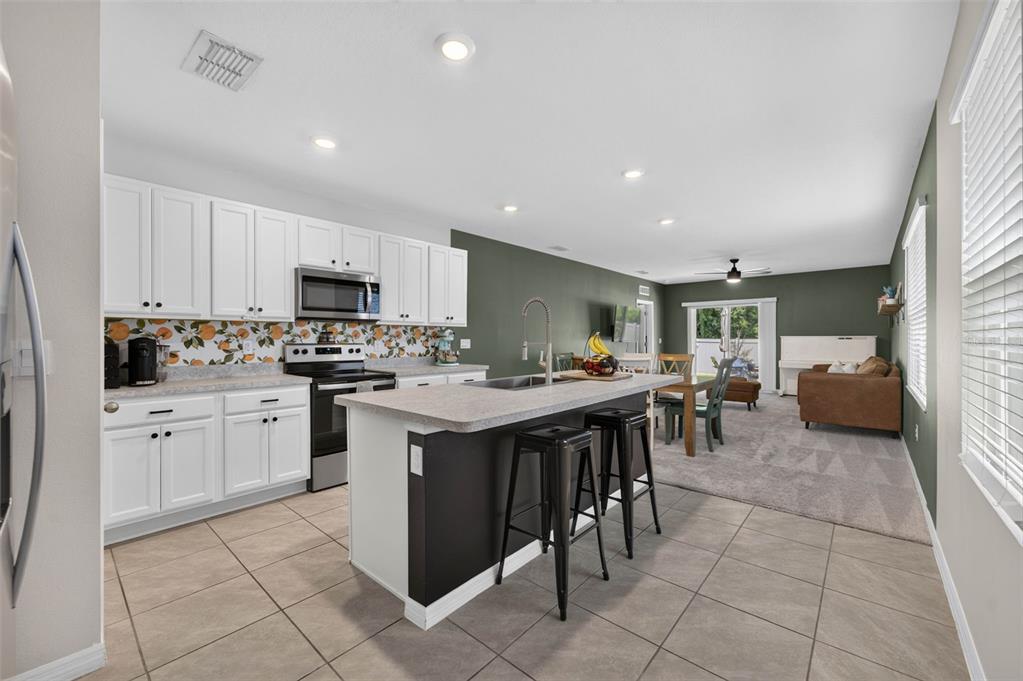 A kitchen with white cabinets, a patterned backsplash, and an island with black bar stools — 2291 DELHI PLACE, SANFORD, FL