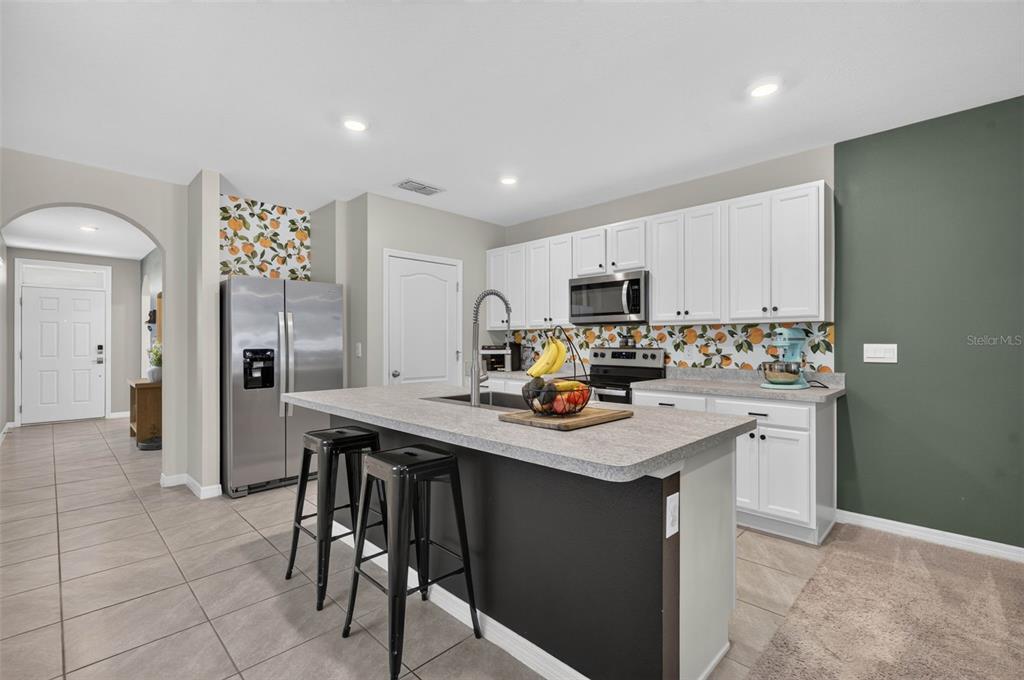 A kitchen features white cabinets, a gray island with black stools, and citrus-patterned wallpaper — 2291 DELHI PLACE, SANFORD, FL