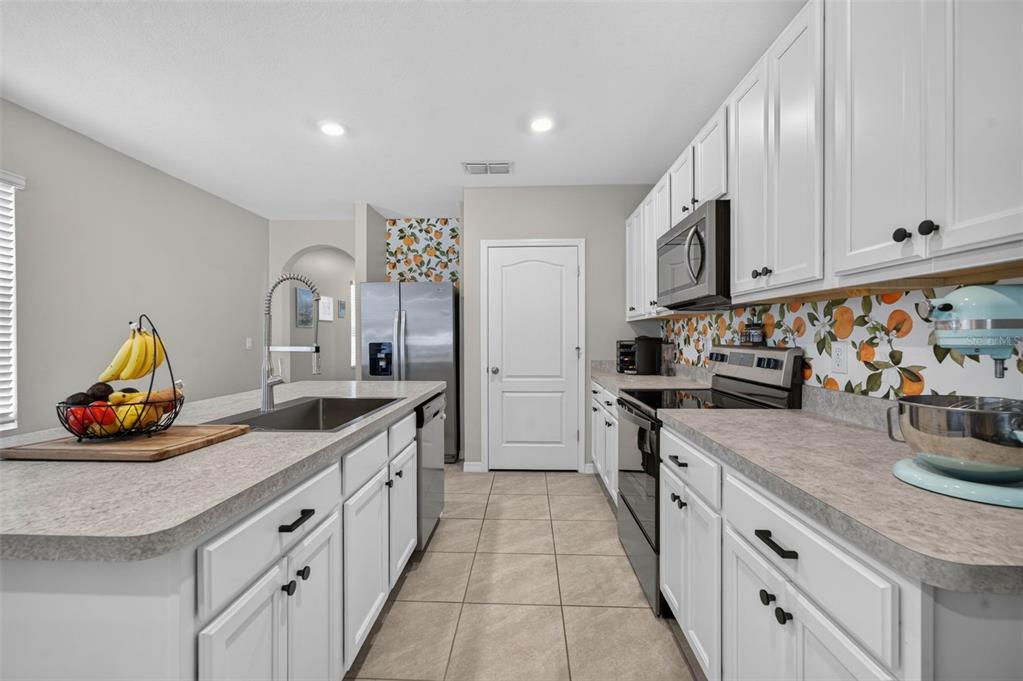 A kitchen features white cabinets, gray countertops, a citrus-patterned backsplash, and a central island — 2291 DELHI PLACE, SANFORD, FL