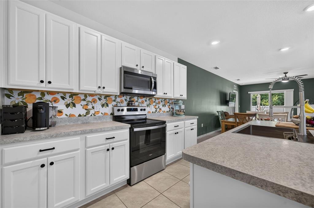 A kitchen features white cabinets, a citrus-patterned backsplash, stainless steel appliances, and a central island — 2291 DELHI PLACE, SANFORD, FL