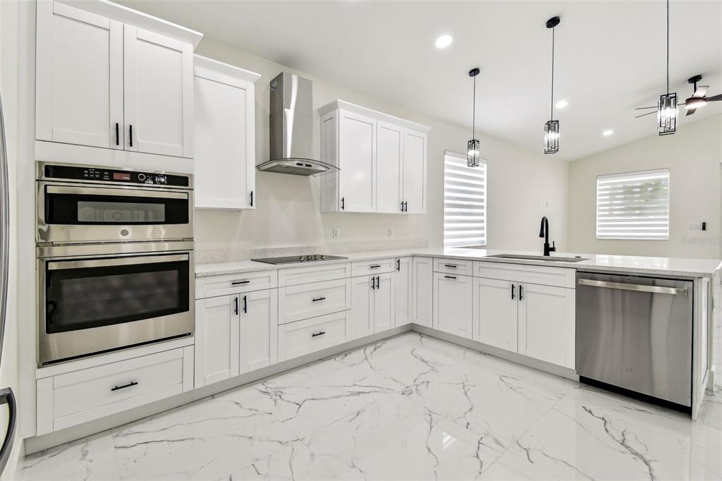 A modern kitchen features white cabinets, stainless steel appliances, and white marble-patterned tile flooring — 7012 N WILLOW AVENUE, TAMPA, FL