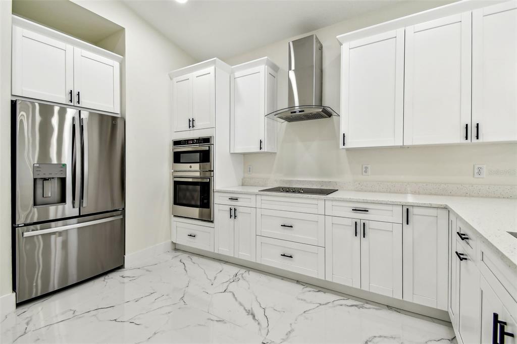 A modern kitchen featuring white cabinets, stainless steel appliances, and white marble-patterned tile flooring — 7012 N WILLOW AVENUE, TAMPA, FL