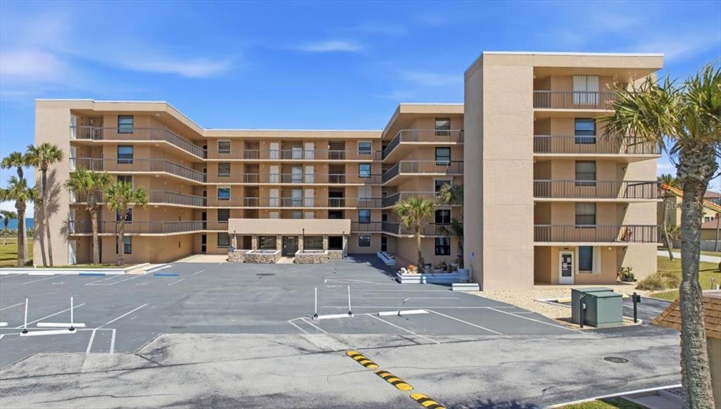 A multi-story beige apartment building features balconies and a large paved parking lot in front — 3360 OCEAN SHORE BOULEVARD UNIT 3070, ORMOND BEACH, FL