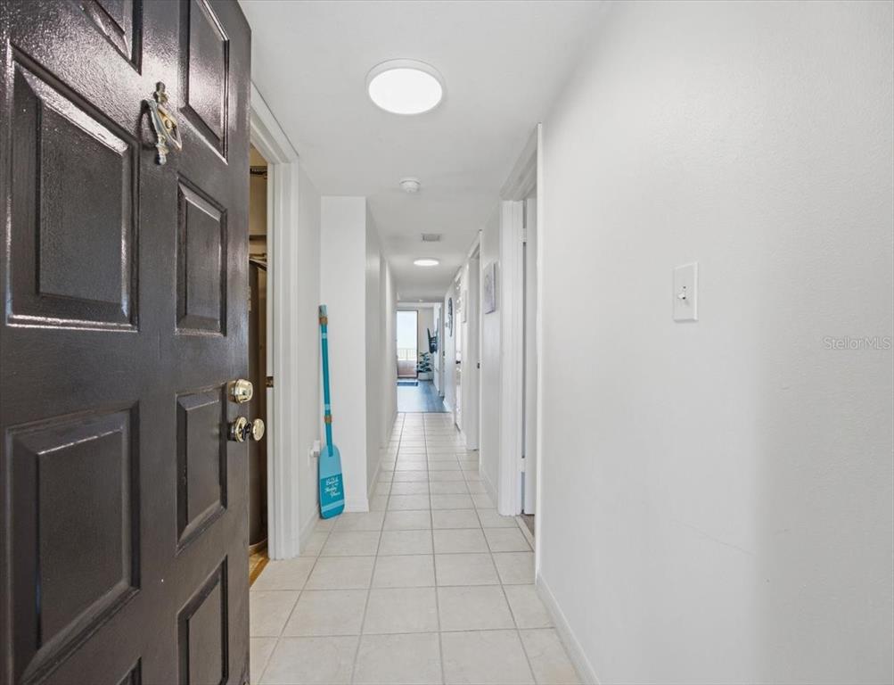 A long hallway with white walls and light-colored tile flooring leads toward a bright doorway — 3360 OCEAN SHORE BOULEVARD UNIT 3070, ORMOND BEACH, FL