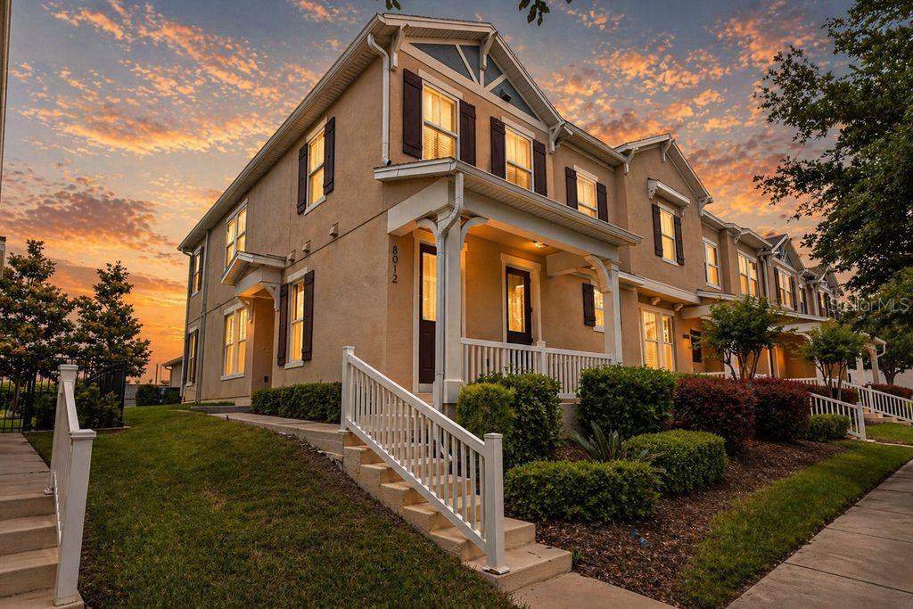 A two-story townhouse with a front porch and tan siding under a sunset sky — 8012 BLUEJACK OAK DRIVE, WINTER GARDEN, FL