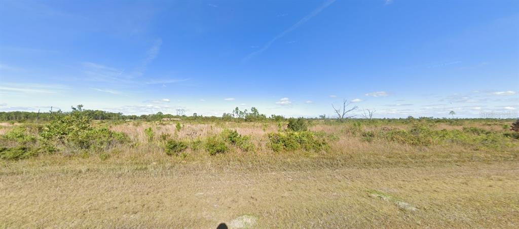 A wide, flat, grassy field under a bright blue sky with scattered low-lying vegetation — 522 PORTULACA DRIVE, INDIAN LAKE ESTATES, FL