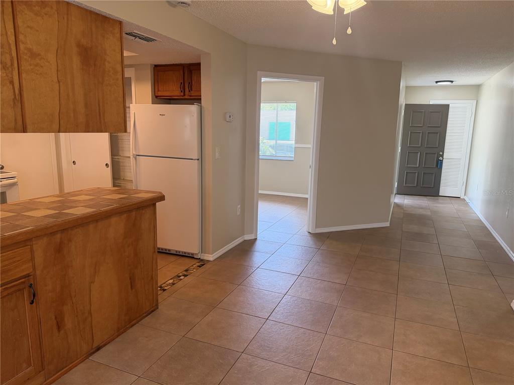 A kitchen with wood cabinets and tile countertops overlooks a tiled living area and entryway — 4239 WOODFIELD AVENUE, HOLIDAY, FL