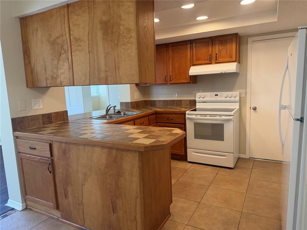 A kitchen featuring wood cabinets, tile countertops, tile flooring, and white appliances — 4239 WOODFIELD AVENUE, HOLIDAY, FL
