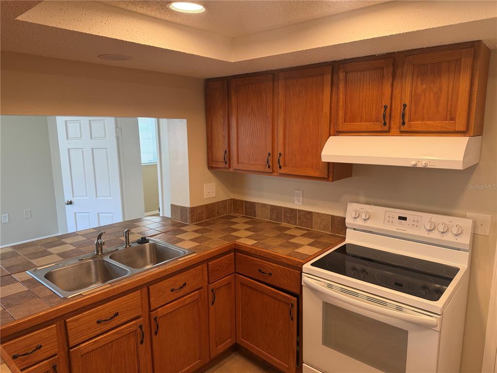 A kitchen features wood cabinets, tile countertops, a double sink, and a white electric stove — 4239 WOODFIELD AVENUE, HOLIDAY, FL