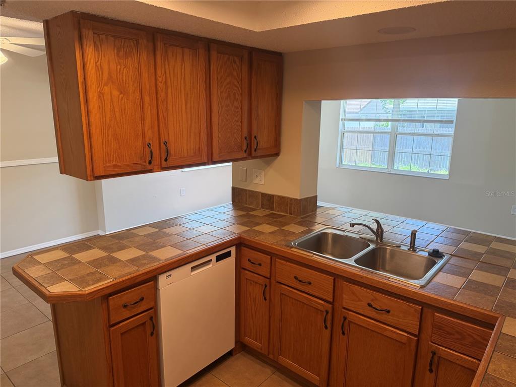A kitchen features oak cabinets, tiled countertops, a double-basin sink, and a white dishwasher — 4239 WOODFIELD AVENUE, HOLIDAY, FL