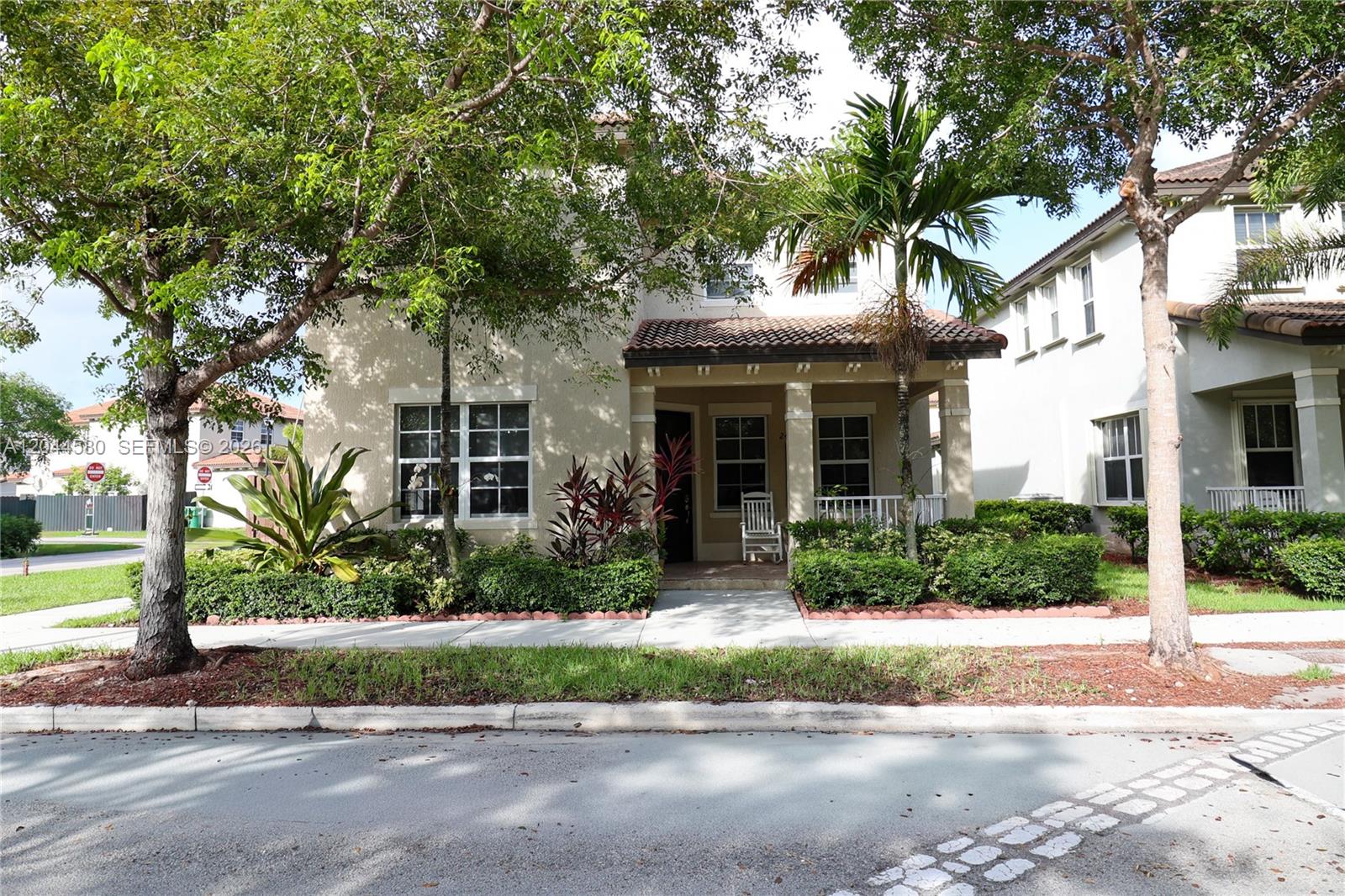 A two-story house with a covered front porch, tan stucco exterior, and mature landscaping — 24623 SW 115th Ct, Homestead FL 33032, HOMESTEAD, FL
