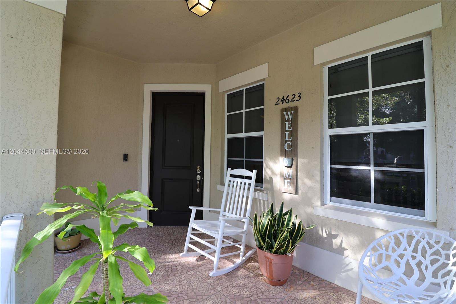 A covered front porch features a dark door, two windows, a rocking chair, and plants — 24623 SW 115th Ct, Homestead FL 33032, HOMESTEAD, FL