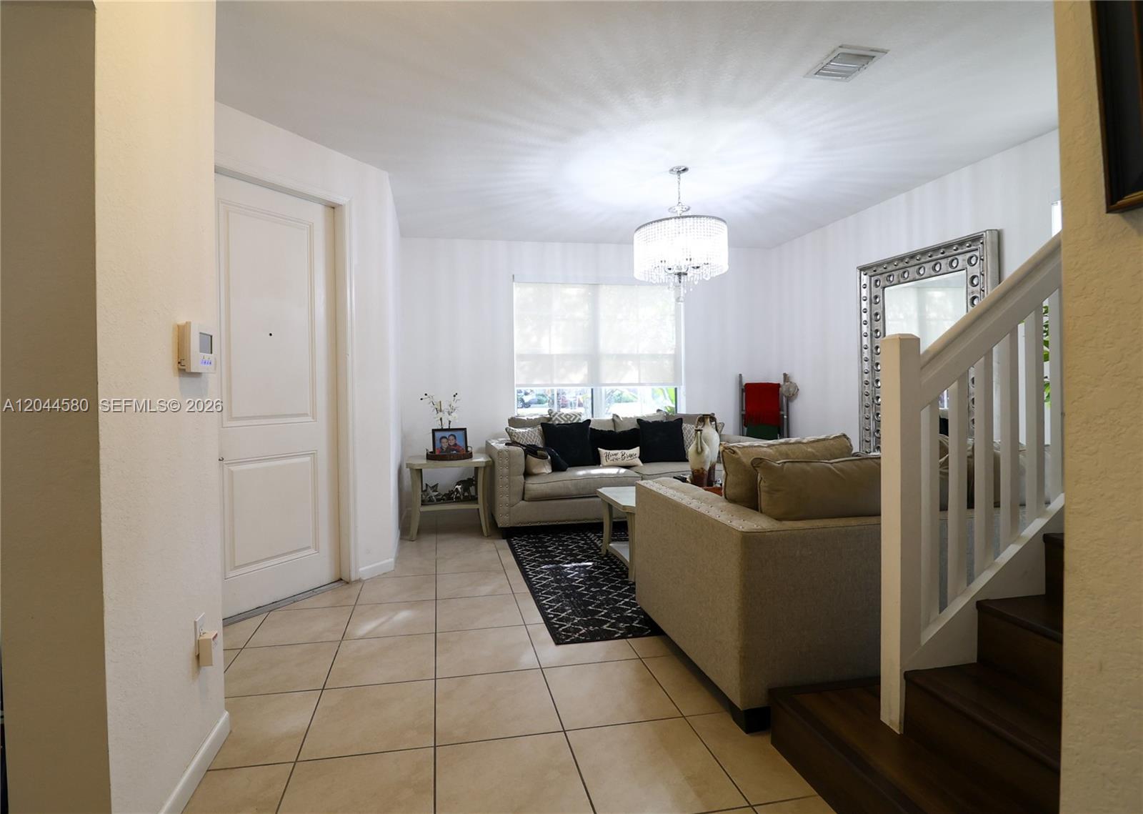 A living room features beige sofas, a crystal chandelier, and tile flooring near a staircase — 24623 SW 115th Ct, Homestead FL 33032, HOMESTEAD, FL