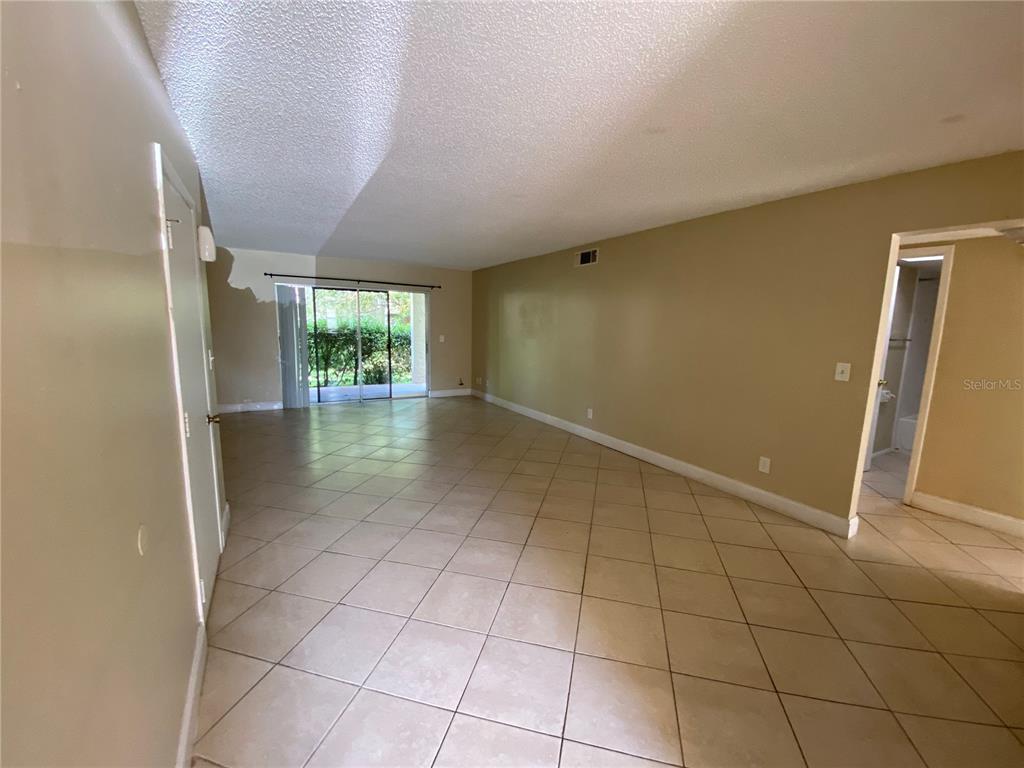 An empty living room features beige tile floors, tan walls, and a sliding glass door — 623 E SAN SEBASTIAN COURT UNIT 623, ALTAMONTE SPRINGS, FL