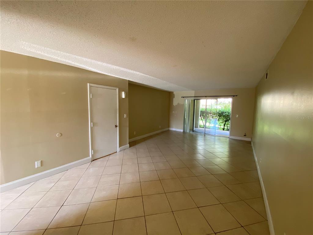 An empty living room features beige walls, tile flooring, and a sliding glass door — 623 E SAN SEBASTIAN COURT UNIT 623, ALTAMONTE SPRINGS, FL