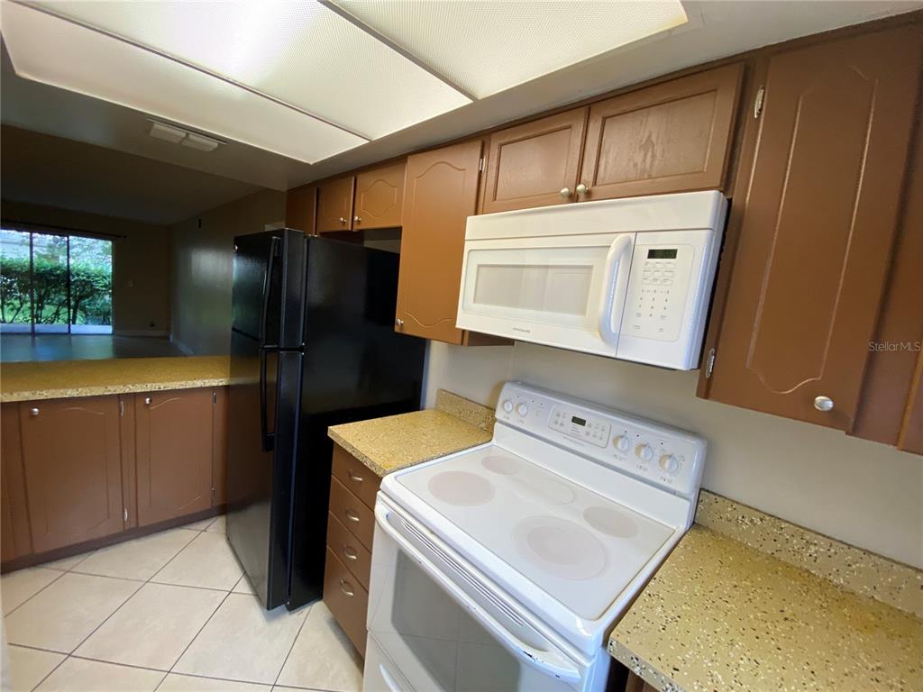 A kitchen features brown cabinets, a black refrigerator, a white stove, and speckled countertops — 623 E SAN SEBASTIAN COURT UNIT 623, ALTAMONTE SPRINGS, FL