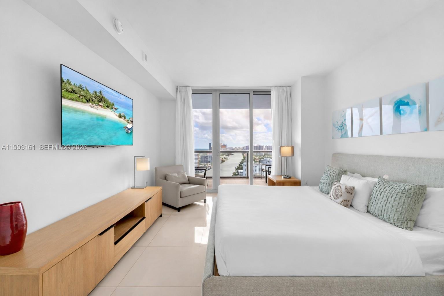 A modern bedroom features a king bed, a wall-mounted television, and a balcony with water views — 2602 E Hallandale Beach Blvd # R2805, Hallandale Beach FL 33009, HALLANDALE BEACH, FL