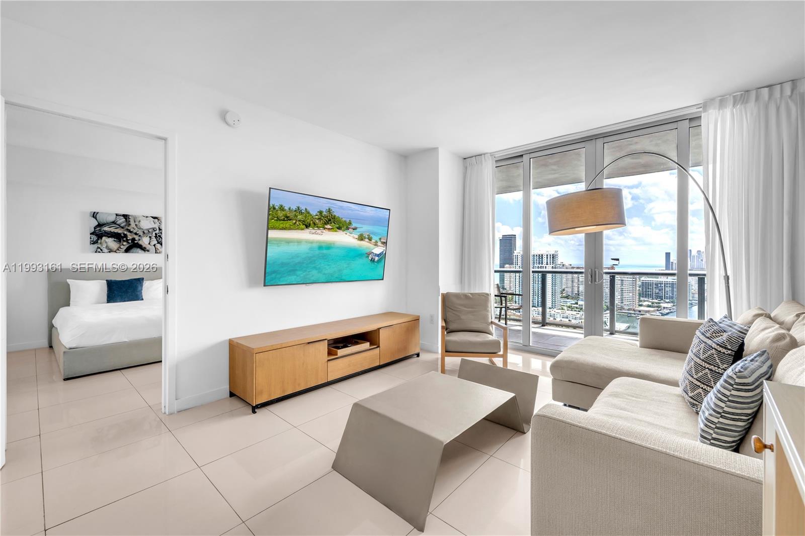 A modern living room features a wall-mounted television, wooden media console, and balcony views — 2602 E Hallandale Beach Blvd # R2805, Hallandale Beach FL 33009, HALLANDALE BEACH, FL