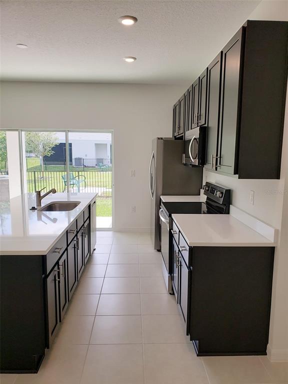 A kitchen features dark cabinets, white countertops, stainless steel appliances, and a large island — 729 MAPLE OAK DRIVE, DELAND, FL