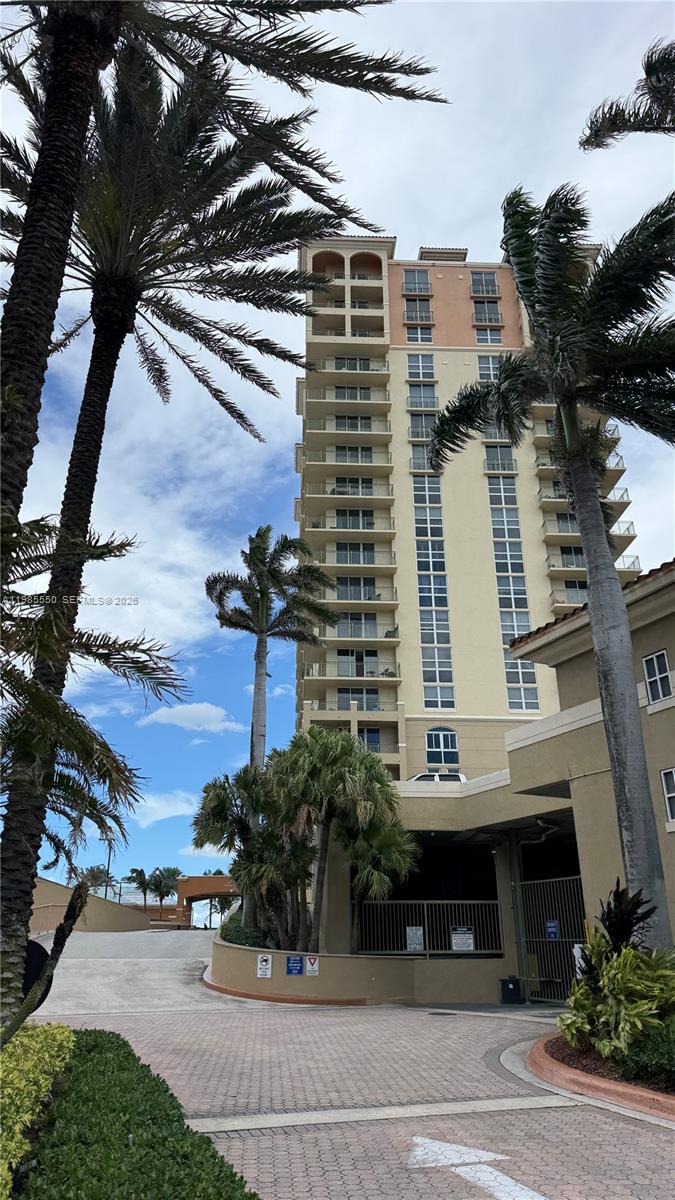 A tall, multi-story residential building stands behind a paved driveway with palm trees — 2080 S Ocean Dr # 905, Hallandale Beach FL 33009, HALLANDALE BEACH, FL