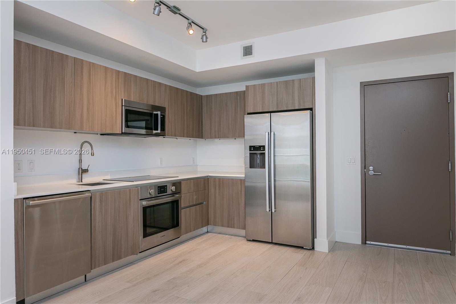 A modern kitchen features wood-grain cabinets, stainless steel appliances, and light-colored flooring — 201 SW 17th Rd # 303, Miami FL 33129, MIAMI, FL