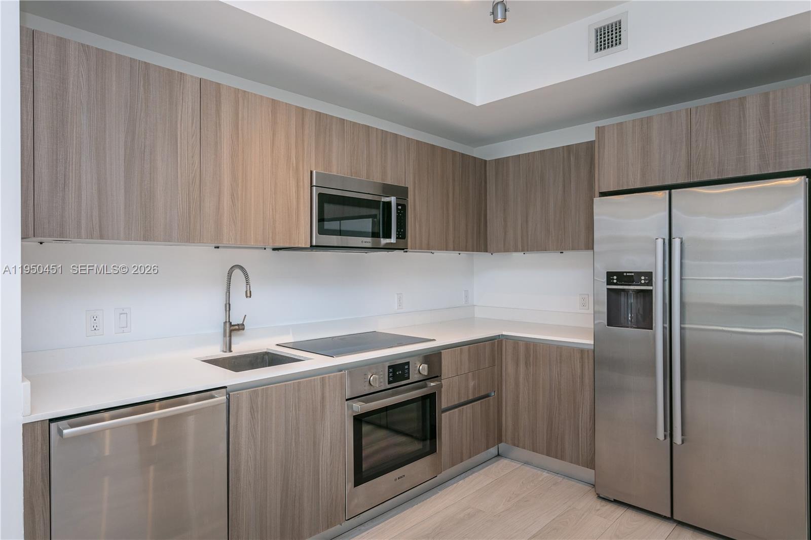 A modern kitchen features wood-grain cabinets, stainless steel appliances, and white countertops — 201 SW 17th Rd # 303, Miami FL 33129, MIAMI, FL
