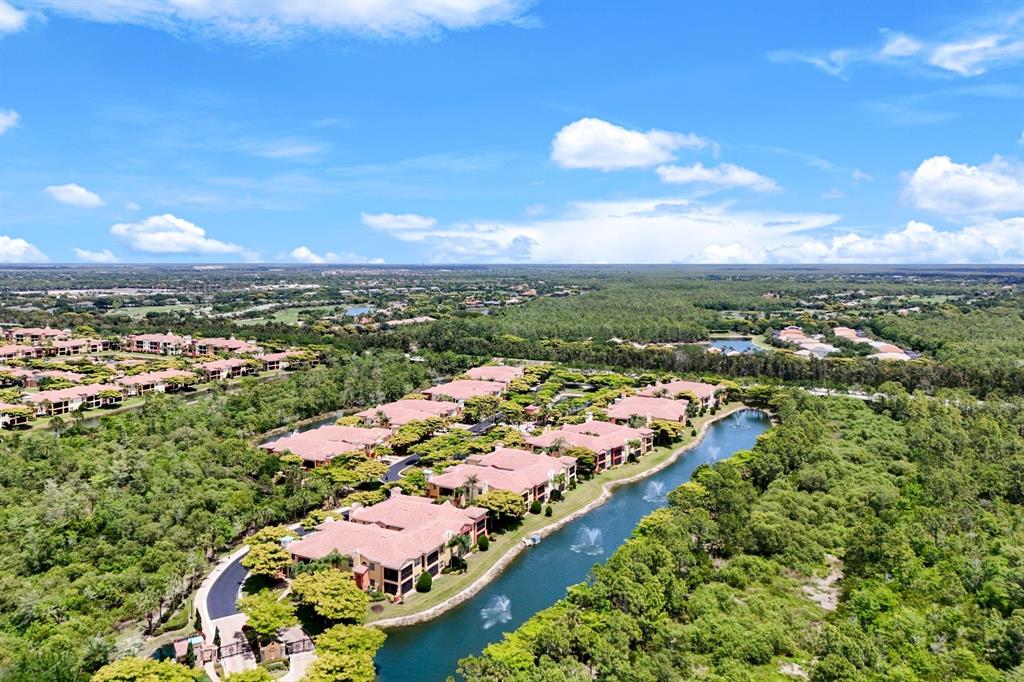 An aerial view shows a residential complex with red-tiled roofs beside a winding pond — 8721 PIAZZA DEL LAGO CIRCLE UNIT 205, ESTERO, FL