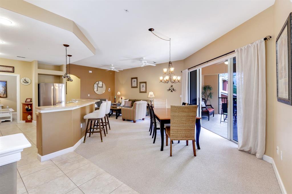 An open-concept living and dining area features a kitchen island, carpeted floors, and sliding doors — 8721 PIAZZA DEL LAGO CIRCLE UNIT 205, ESTERO, FL
