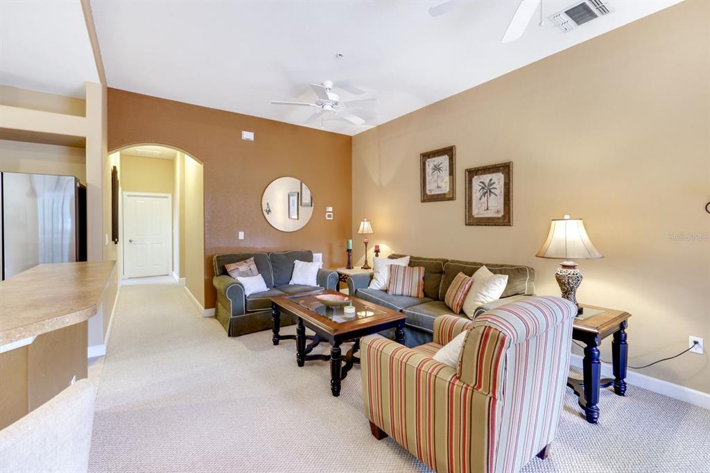 A living room features beige and brown walls, carpeted floors, and a seating area — 8721 PIAZZA DEL LAGO CIRCLE UNIT 205, ESTERO, FL
