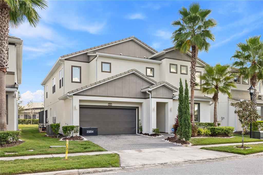 A two-story suburban house with a gray garage, beige stucco siding, and palm trees — 2694 CALISTOGA AVENUE, KISSIMMEE, FL