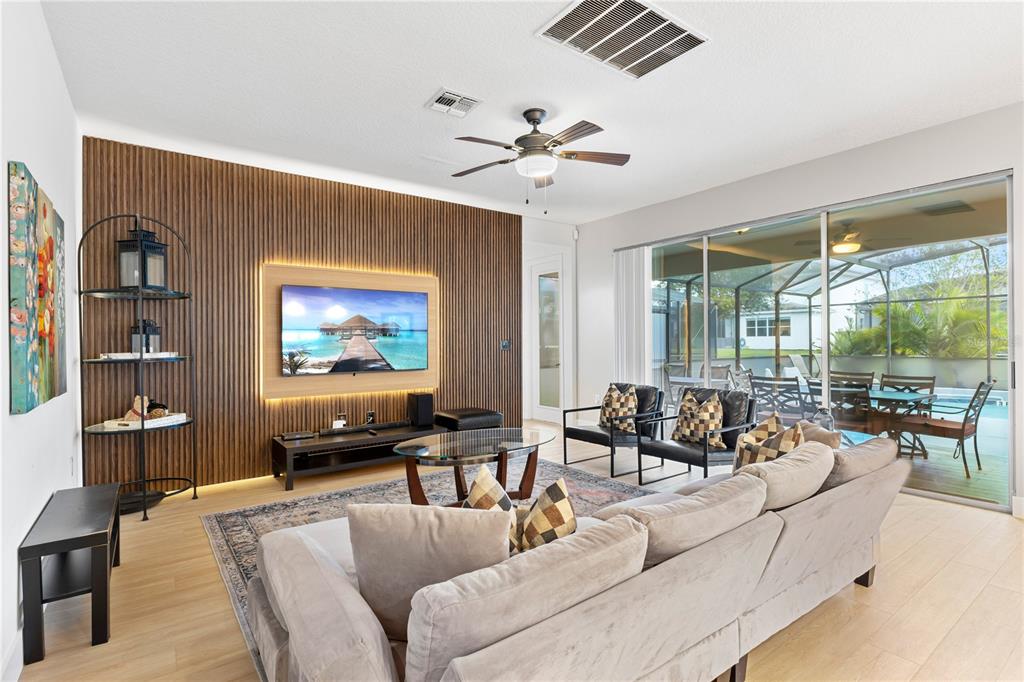 A living room features a wood-slat accent wall, a mounted television, and sliding glass doors — 2694 CALISTOGA AVENUE, KISSIMMEE, FL