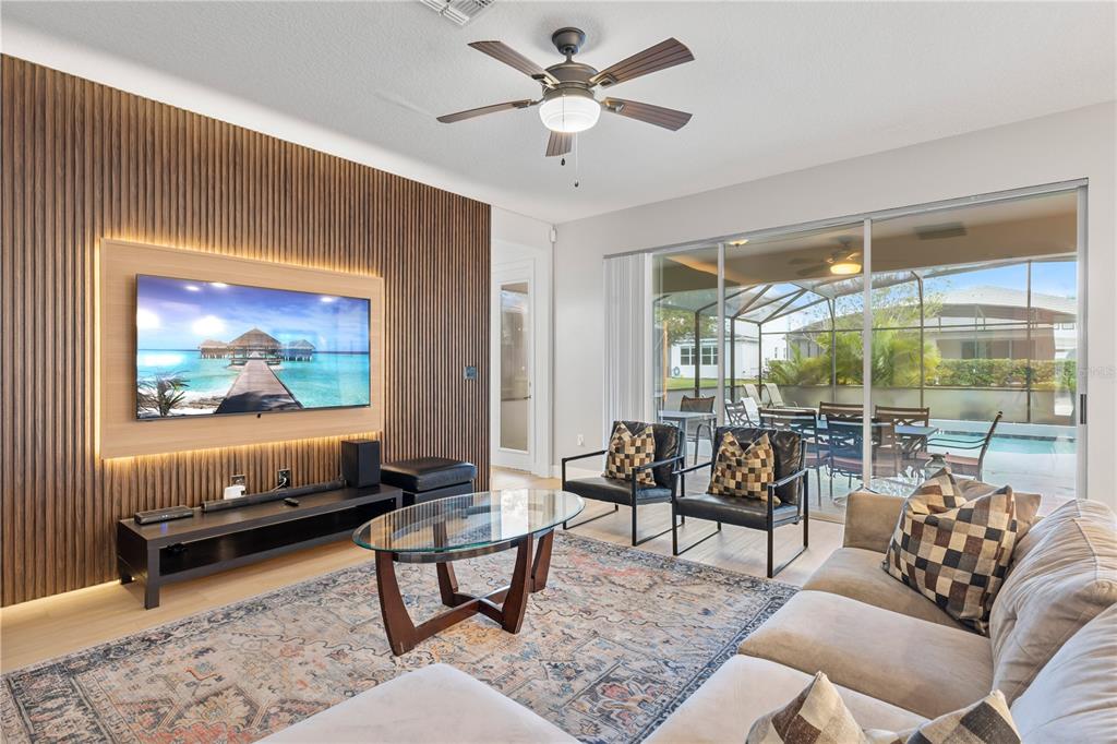 A living room features a wood-slatted accent wall, a television, and a glass sliding door — 2694 CALISTOGA AVENUE, KISSIMMEE, FL