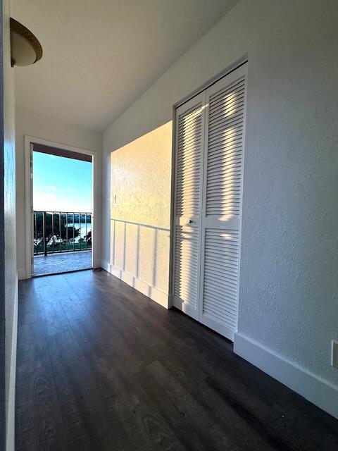 A hallway with dark wood-look flooring, white louvered closet doors, and a door to a balcony — 4570 NW 18th Avenue # 609, Deerfield Beach FL 33064, DEERFIELD BEACH, FL