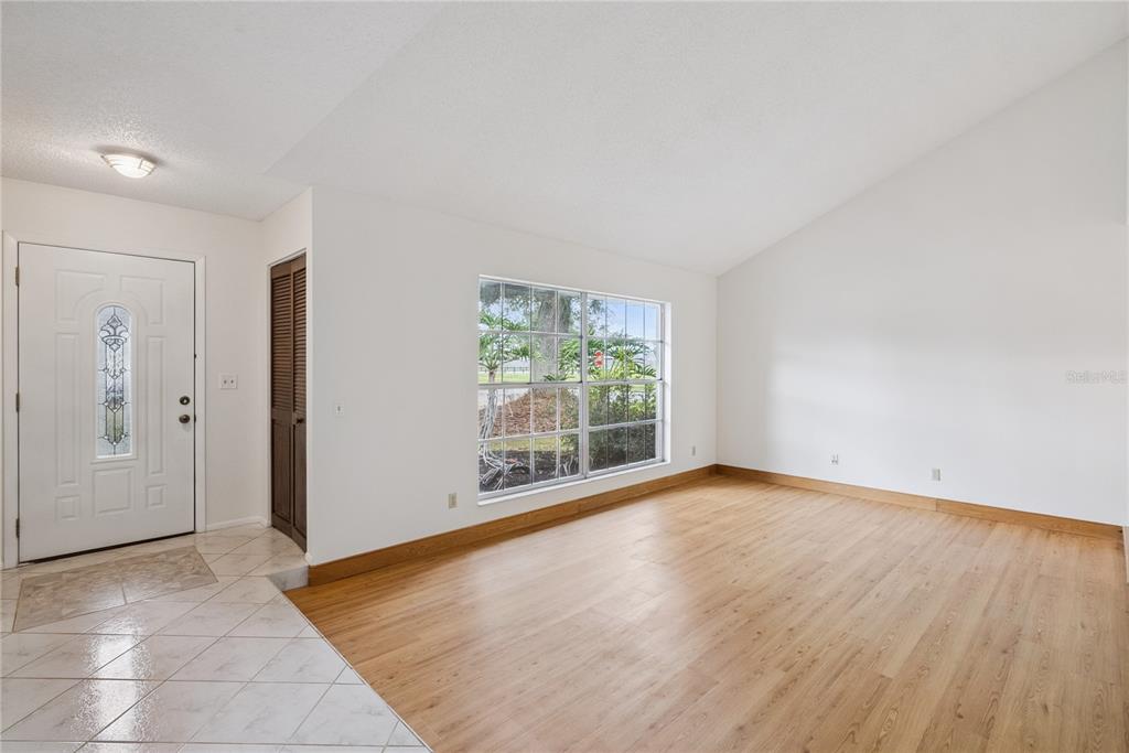 An empty living room features light wood flooring, white walls, a vaulted ceiling, and a window — 1298 MADELENA AVENUE, WINTER SPRINGS, FL
