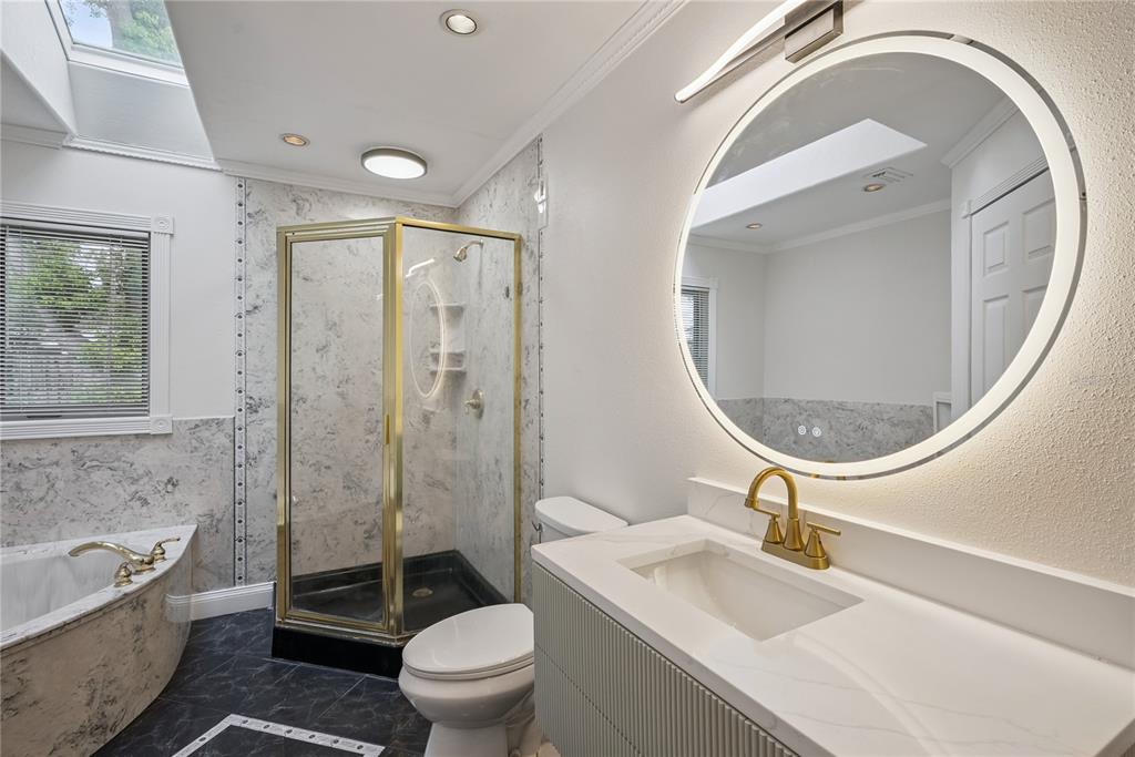 A bathroom features a marble-tiled shower, a soaking tub, a vanity, and a round mirror — 1298 MADELENA AVENUE, WINTER SPRINGS, FL