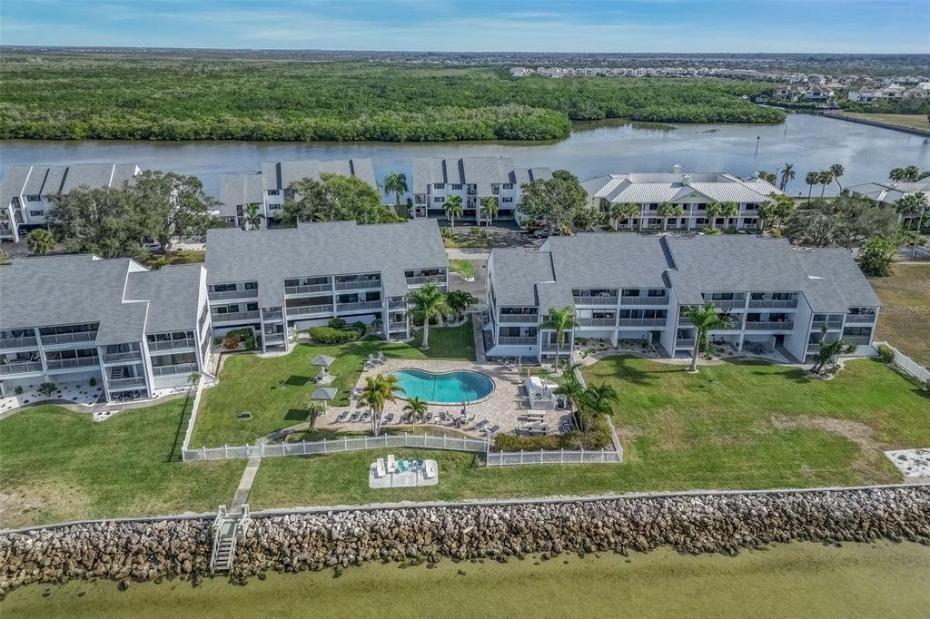 An aerial view shows waterfront apartment buildings with a central swimming pool and grassy lawn — 803 BAHIA DEL SOL DRIVE UNIT B, RUSKIN, FL