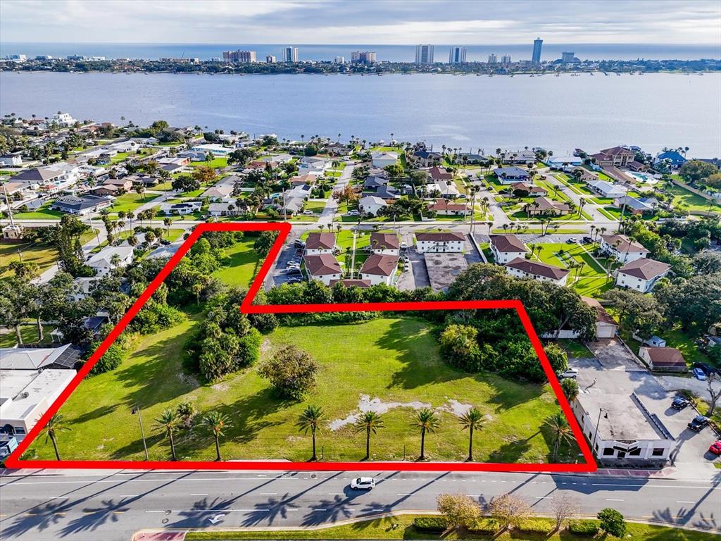 An aerial view shows a vacant, L-shaped grassy lot outlined in red along a road — 1771 S RIDGE WOOD AVENUE, SOUTH DAYTONA, FL