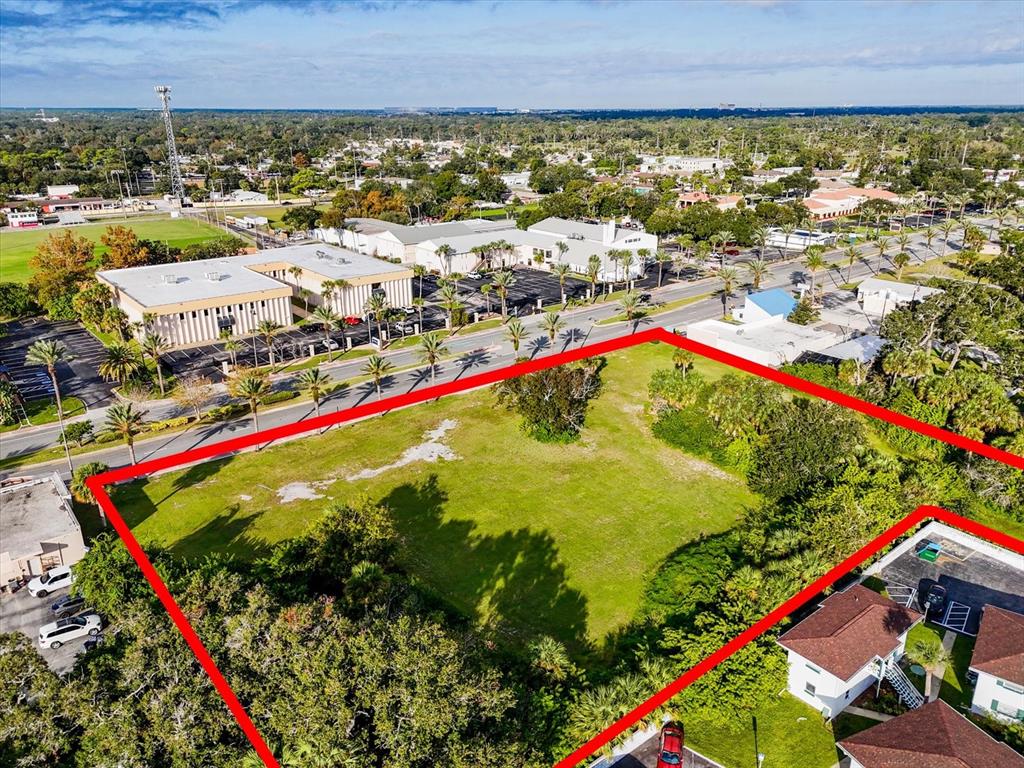 An aerial view shows a vacant, rectangular grassy lot outlined in red near a road — 1771 S RIDGE WOOD AVENUE, SOUTH DAYTONA, FL