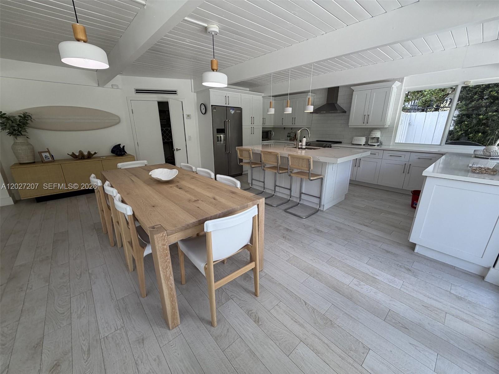 A bright, open-concept kitchen and dining area features white cabinetry, wood flooring, and pendant lighting — 665 Allendale Rd, Key Biscayne FL 33149, KEY BISCAYNE, FL