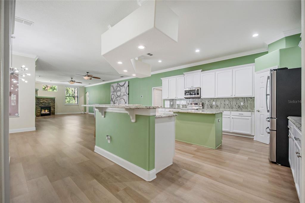 An open living area features light wood flooring, decorative columns, and a view of a pool — 8615 WARWICK SHORE CROSSING, ORLANDO, FL