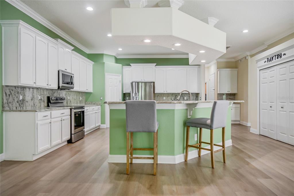 A kitchen features white cabinets, green walls, a central island with two chairs, and flooring — 8615 WARWICK SHORE CROSSING, ORLANDO, FL
