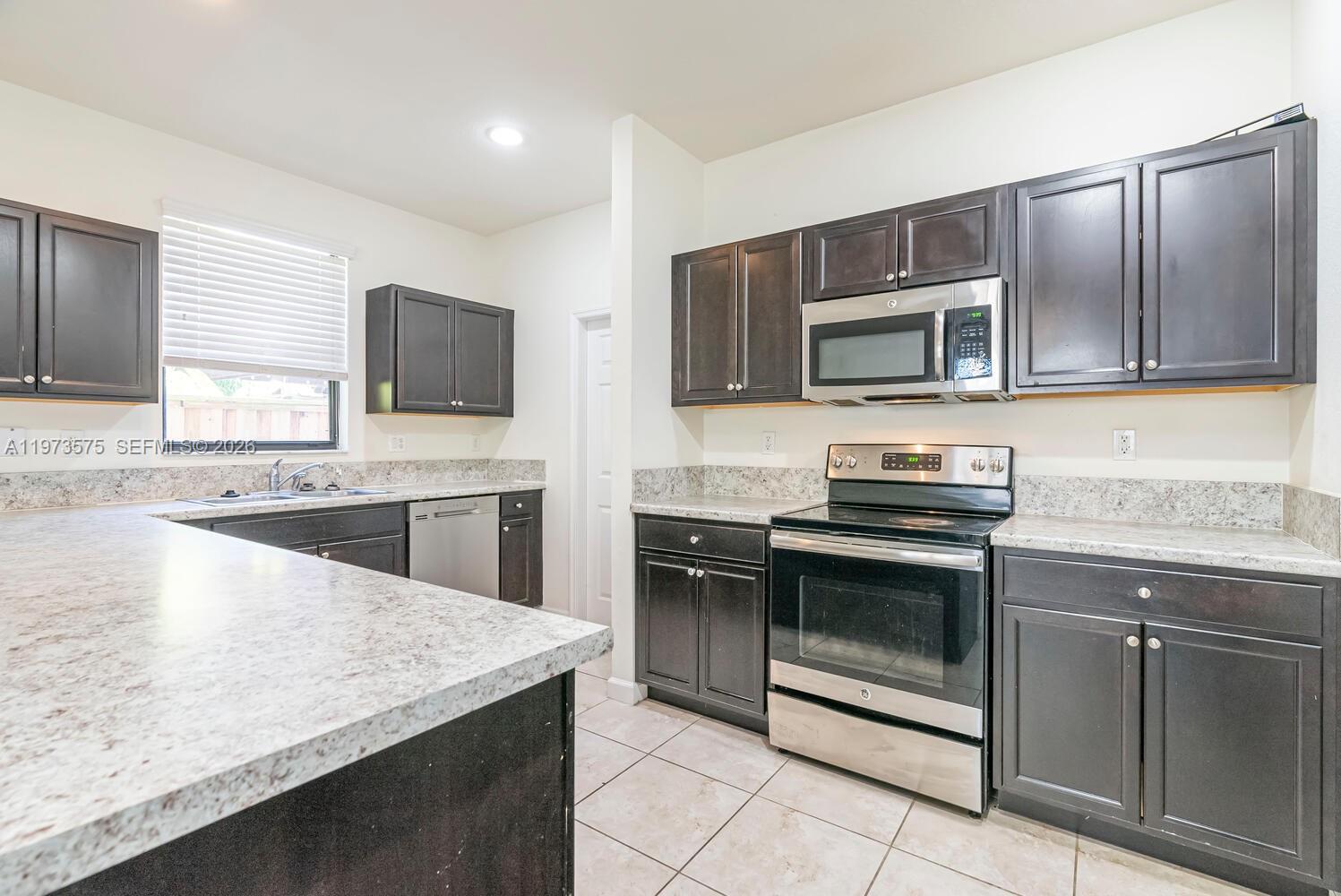 A kitchen features dark wood cabinets, stainless steel appliances, and speckled granite countertops — 516 SE 35th Ter, Homestead FL 33033, HOMESTEAD, FL