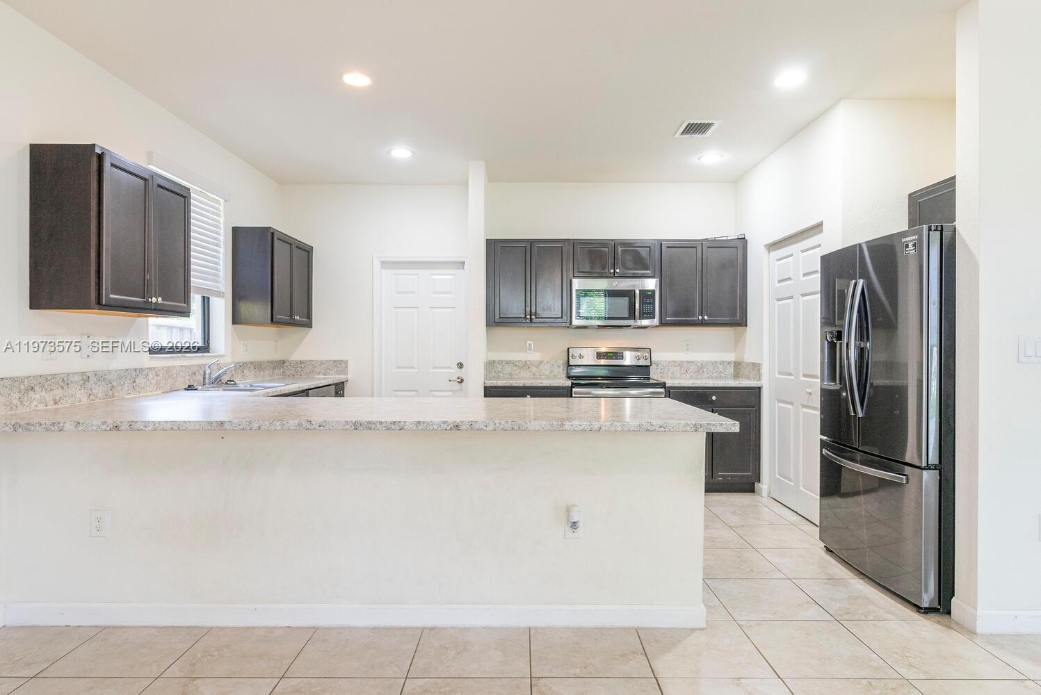 A kitchen features dark wood cabinets, granite countertops, stainless steel appliances, and tile flooring — 516 SE 35th Ter, Homestead FL 33033, HOMESTEAD, FL