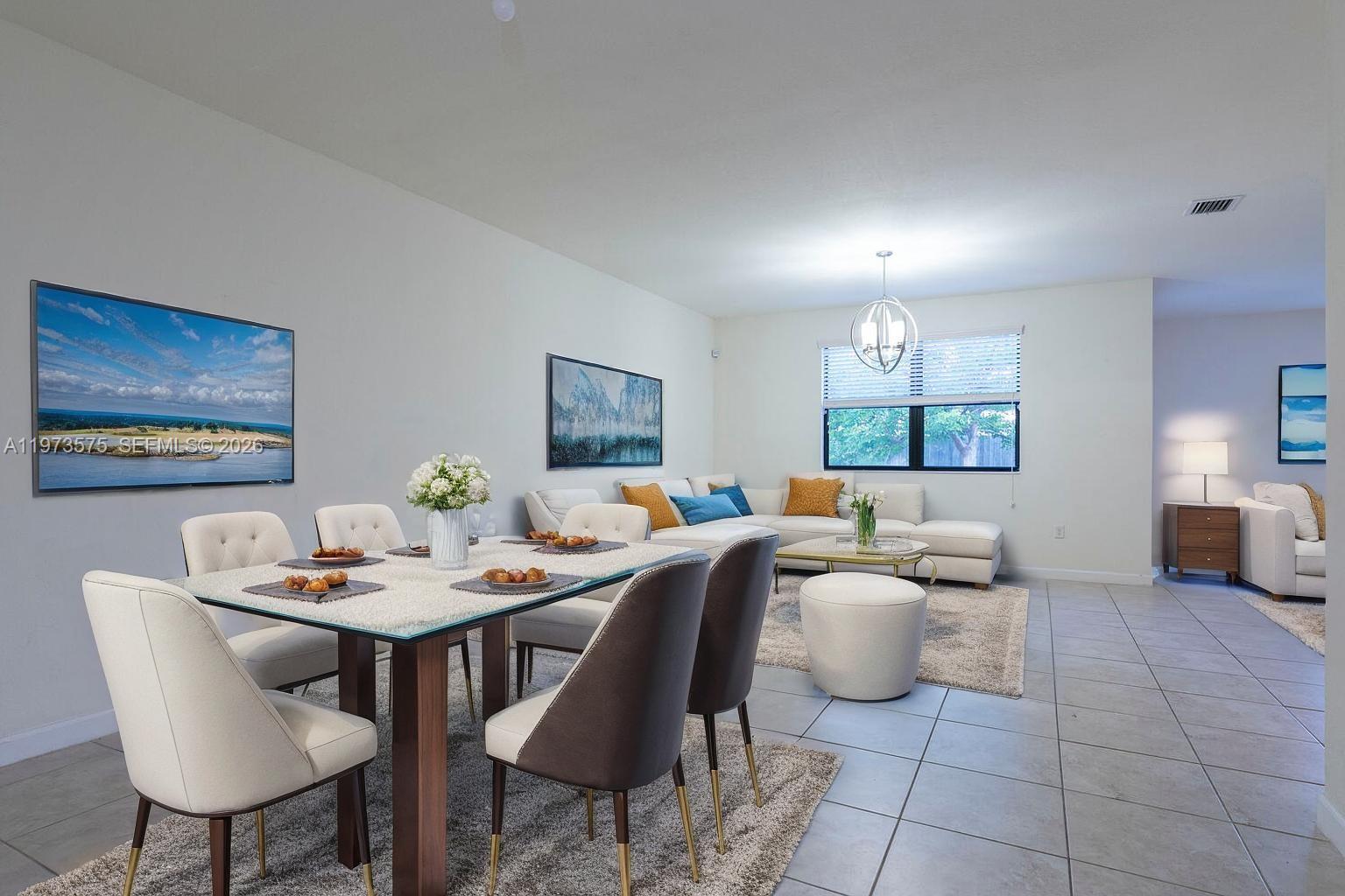This open-concept living and dining room features tile flooring, neutral walls, and modern furniture — 516 SE 35th Ter, Homestead FL 33033, HOMESTEAD, FL