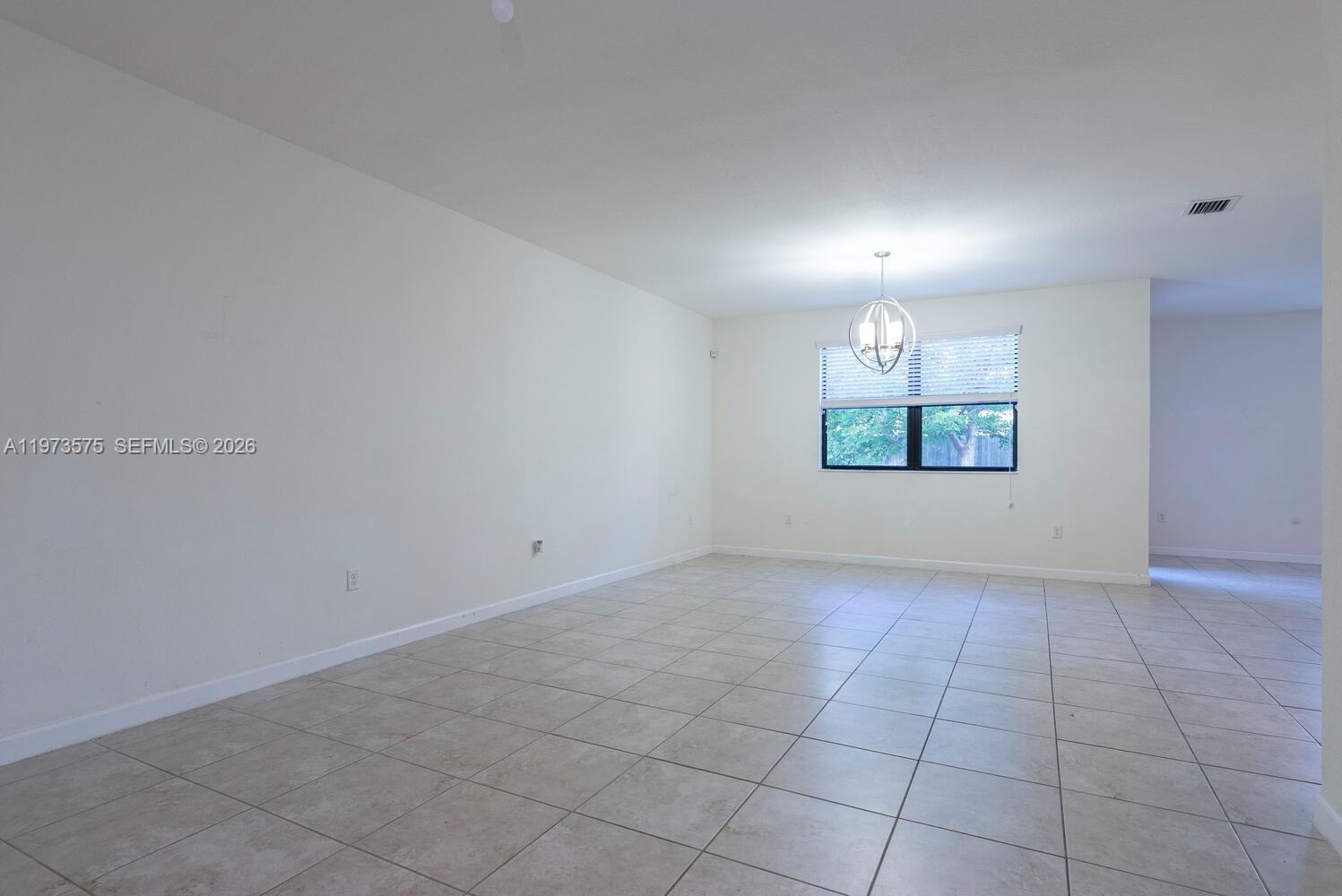 An empty room features white walls, light-colored tile flooring, and a central hanging light fixture — 516 SE 35th Ter, Homestead FL 33033, HOMESTEAD, FL