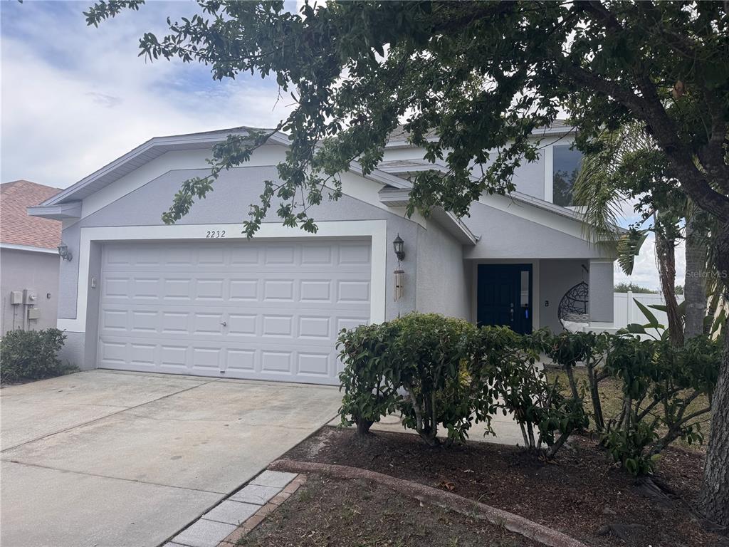 A light-colored two-story house features a two-car garage, a front entrance, and mature landscaping — 2232 COLVILLE CHASE DRIVE, RUSKIN, FL