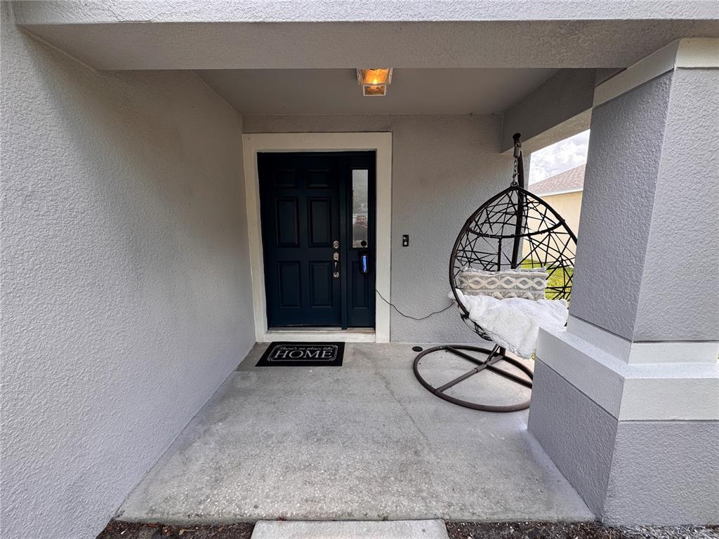 A covered concrete entryway features a dark blue front door and a hanging egg chair — 2232 COLVILLE CHASE DRIVE, RUSKIN, FL